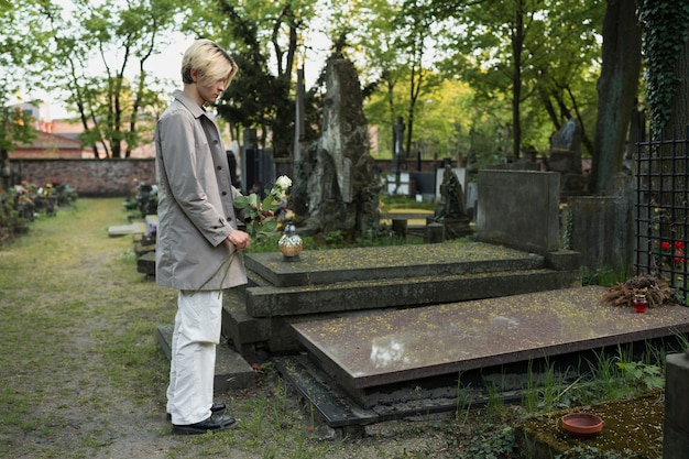 Mann mit weißen Rosen auf dem Friedhof neben Grab