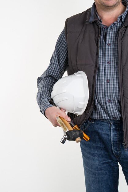 Mann mit Werkzeugen in der Tasche und einem Bauhelm in der Hand vor einem schlichten weißen Hintergrund.