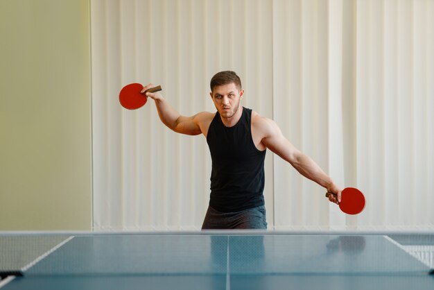 Mann mit zwei Schlägern, die drinnen Tischtennis spielen.