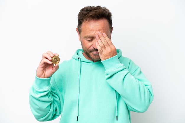 Mann mittleren Alters, der einen Bitcoin über isoliertem Hintergrund mit müdem und krankem Ausdruck hält