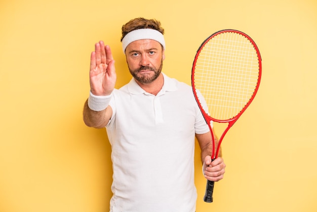 Mann mittleren Alters, der ernsthaft aussieht und eine offene Handfläche zeigt, die ein Stoppgesten-Tenniskonzept macht