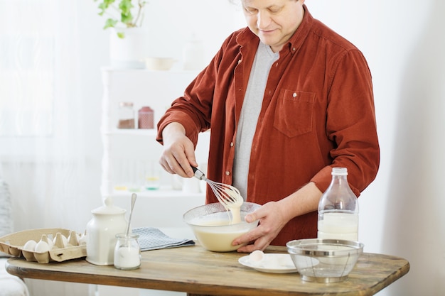 Mann mittleren Alters, der Pfannkuchenteig auf weißer Küche knetet