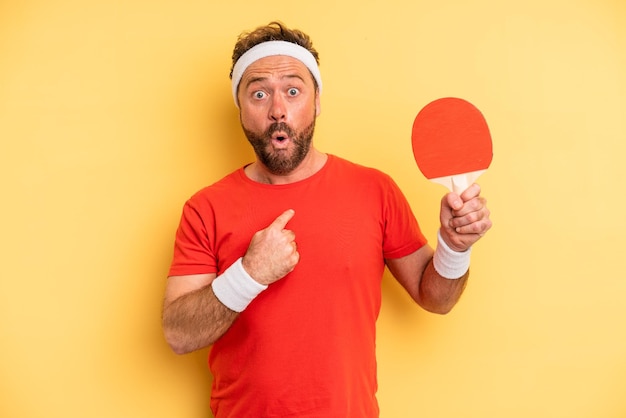 Mann mittleren Alters, der schockiert und überrascht mit weit geöffnetem Mund aussieht und auf sich selbst zeigt. Ping-Pong-Konzept