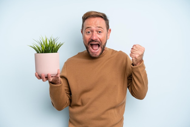 Foto mann mittleren alters, der sich schockiert fühlt, lacht und erfolg feiert. blumentopfkonzept