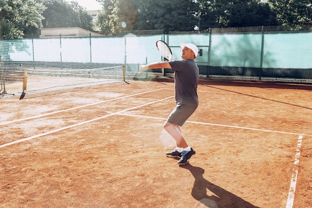 Mann mittleren Alters, der Tennis auf Tennis im Freien spielt, eingereicht