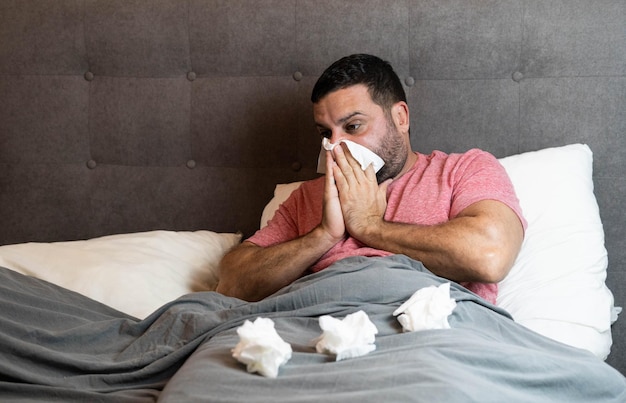 Mann mittleren Alters liegt krank mit Grippesymptomen im Bett.