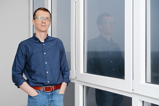 Mann mittleren Alters steht am frühen Morgen mit den Händen in den Taschen auf dem Balkon