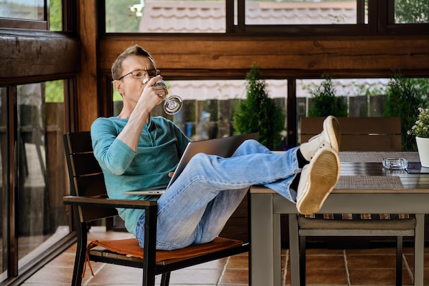 Mann mittleren Alters trinkt Wein, während er Online-Übertragungen auf dem Laptop ansieht