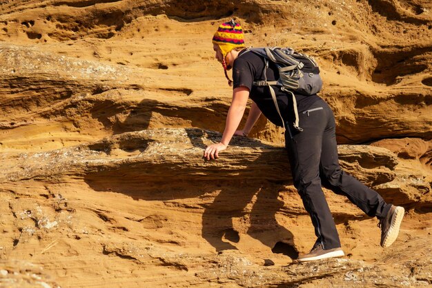 Mann mutiger rothaariger Bartkletterbouldersteinfelstourist klettert mit Rucksack in einem schwarzen T-Shirt und einem lustigen Hut aus Yakwolle aus Nepal hinauf