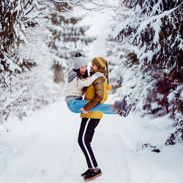 Mann nimmt Frau auf seinen Armen in einem Winterwald mit Schnee