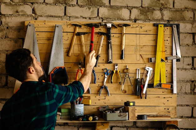 Mann nimmt Hammer von der Wand mit Werkzeugen