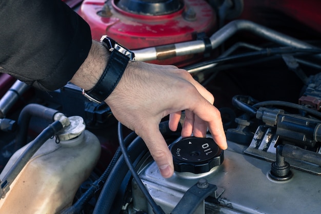 Mann öffnet den Öldeckel von einem Automotor.