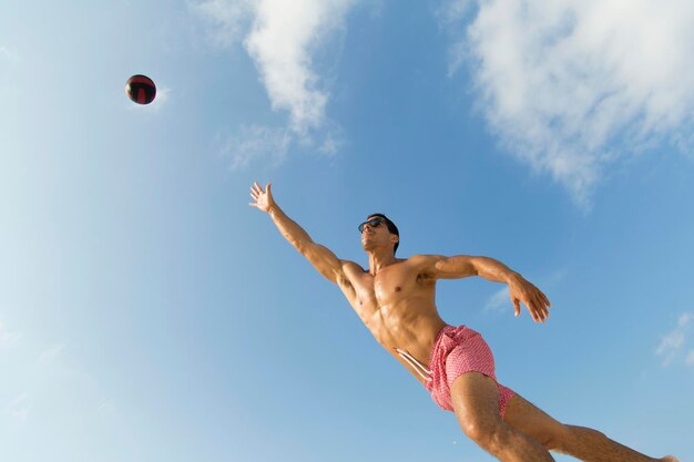 Mann ohne Hemd spielt Volleyball gegen den Himmel