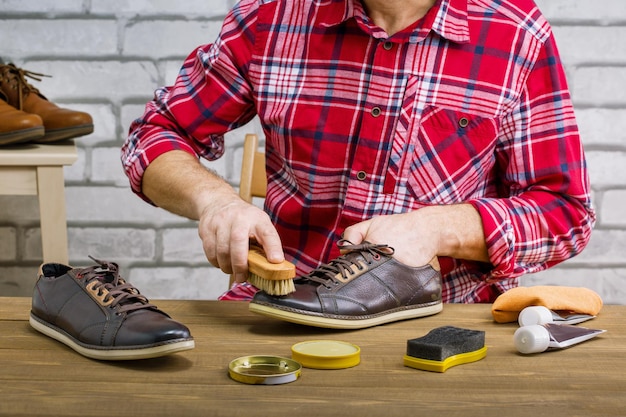 Mann poliert Lederschuhe mit Bürste auf Holztisch des Arbeitsplatzes. Kleinbetrieb.