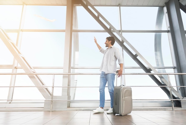 Mann Reisenden mit Gepäck im Flughafen spazieren und zum Fenster winken