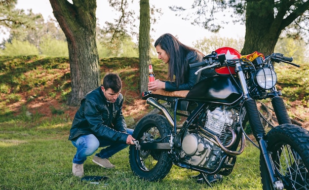 Mann repariert sein Motorrad, während seine Freundin ihn ansieht