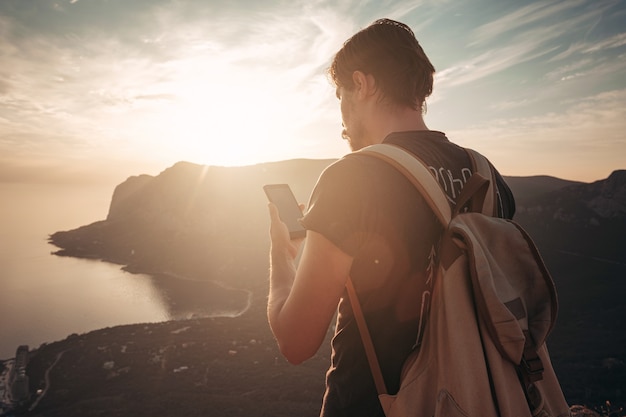 Mann Rucksacktourist mit Smartphone entspannen auf Berggipfel allein reisen. Lifestyle Aktivurlaub Moderne Technologie Millennials Konzept. Herrlicher Tagesanbruch. Mock-up-Text.