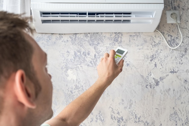 Mann schaltet die Klimaanlage für eine angenehme Temperatur mit der Fernbedienung zu Hause im heißen Sommer ein