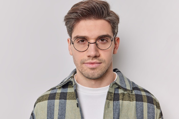 Mann schaut direkt ohne emotionen hört wichtige nachrichten trägt runde brille und kariertes hemd einzeln auf weiß denkt über etwas wichtiges nach