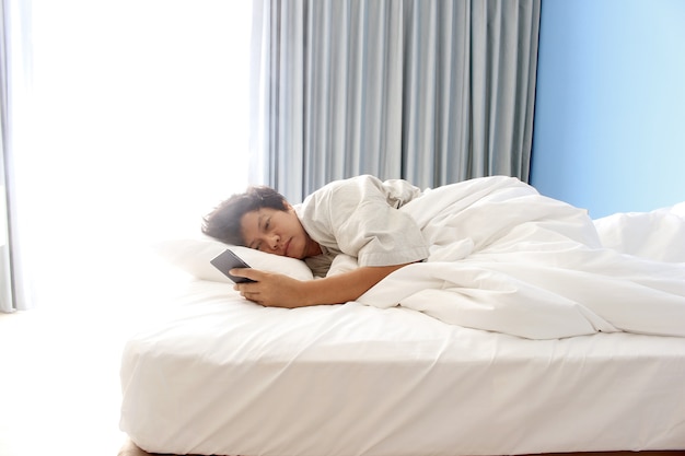 Foto mann schläft im bett und hält ein smartphone