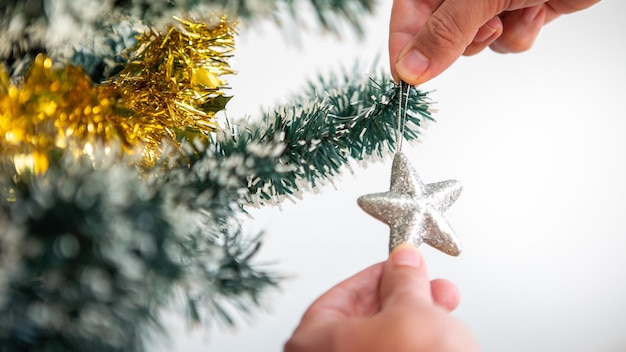 Mann schmückt Weihnachtsbaum mit silbernen Sternen im Wohnzimmerhaus. Frohe Weihnachten und ein glückliches neues Jahr-Konzept. Menschen setzen Weihnachtsschmuck auf Fichtenzweige. Familienfreundliche Momente