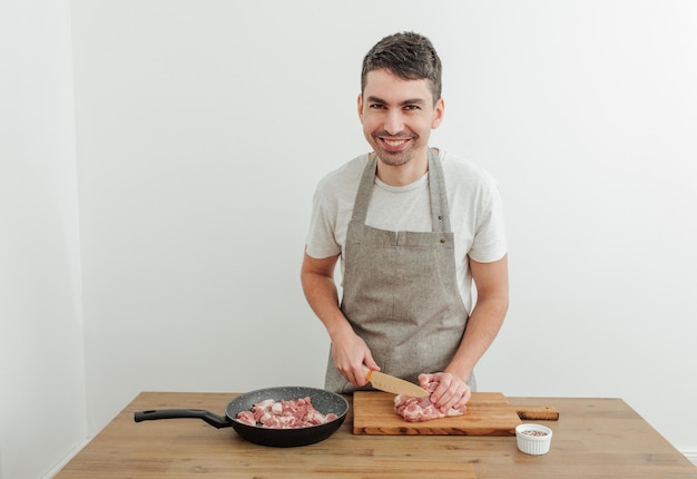 Mann schneidet Fleisch mit einem Messer auf einem Schneidebrett Holztisch Bratpfanne mit frischem Schweinefleisch