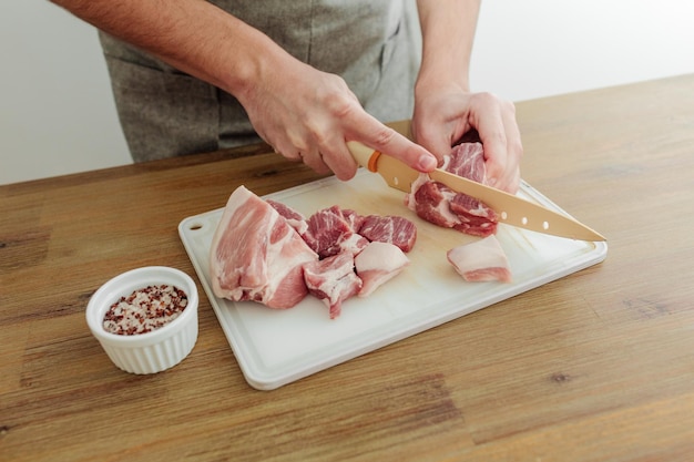 Mann schneidet Fleisch mit einem Messer auf einem Schneidebrett Holztisch Frisches Schweinefleisch