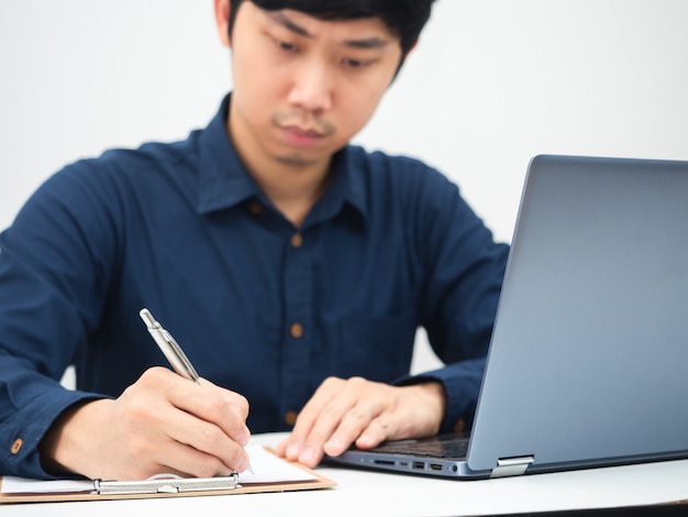 Mann schreibt Dokumenttafel den Tisch und verwendet Laptop, der von zu Hause aus arbeitet