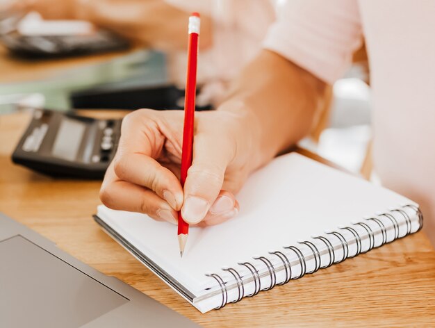 Mann schreibt Geschäftsinformationen in Notizbuch am Arbeitsplatz im Büro mit Taschenrechner und Laptop