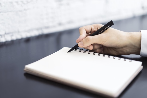 Mann schreibt mit einem Stift in Tagebuch in einem sonnigen Büro, Geschäfts- und Bildungskonzept aus nächster Nähe