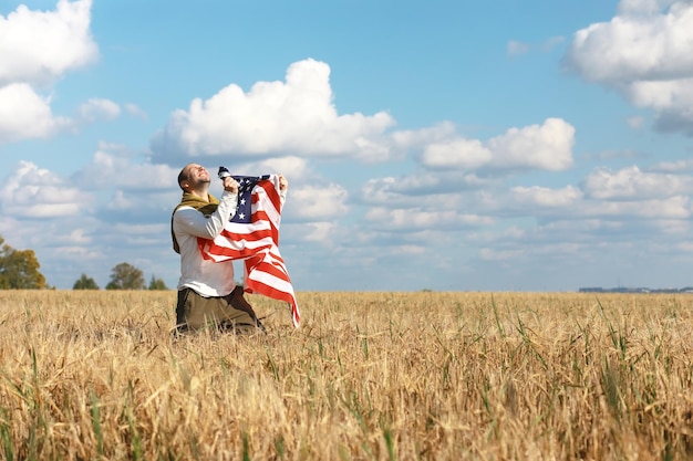 Mann schwenkt die amerikanische Flagge, die im landwirtschaftlichen Bereich der Grasfarm steht, Feiertage, Patriotismus, Stolz, Freiheit, politische Parteien, Einwanderer