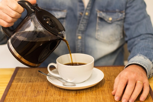 Mann serviert einen gefilterten Kaffee in einer weißen Tasse auf einem Tisch