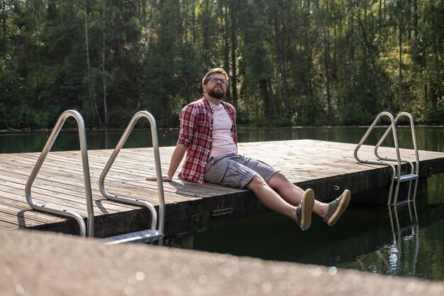 Mann sitzt am Rand eines Holzstegs und blickt nachdenklich gegen einen ruhigen Waldsee
