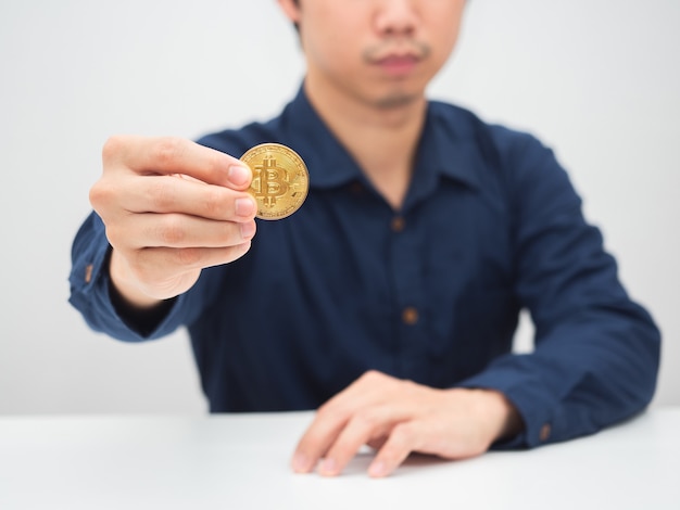 Mann sitzt am Schreibtisch und zeigt Goldbitcoin in der Hand