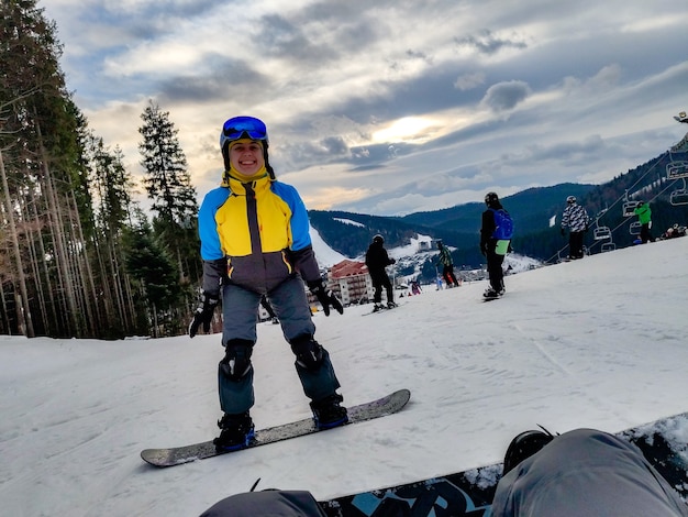 Mann sitzt am verschneiten Hügel mit Snowboard glückliche Frau vor Winterskigebiet