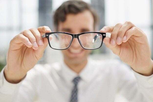 Mann sitzt an einem Tisch und blickt durch eine Brille in die Kamera