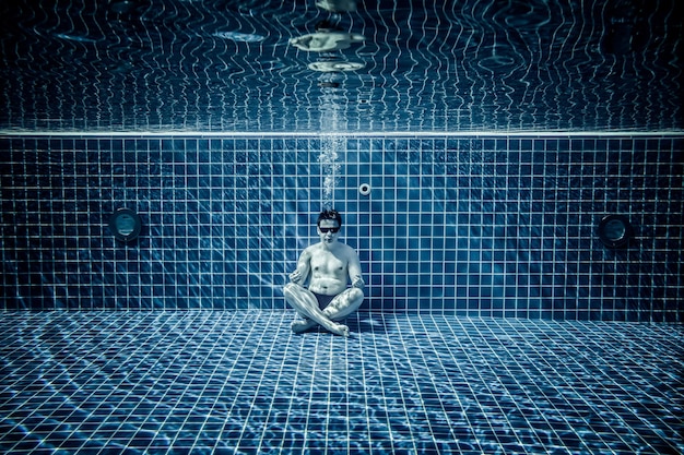 Mann sitzt auf dem Boden des Schwimmbeckens unter Wasser