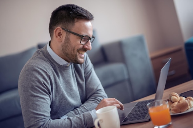 Mann sitzt auf dem Boden, während er zu Hause Laptop anschaut