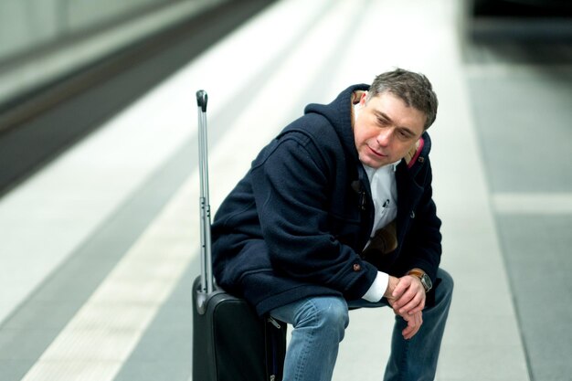 Foto mann sitzt auf dem gepäck am bahnhofssteig