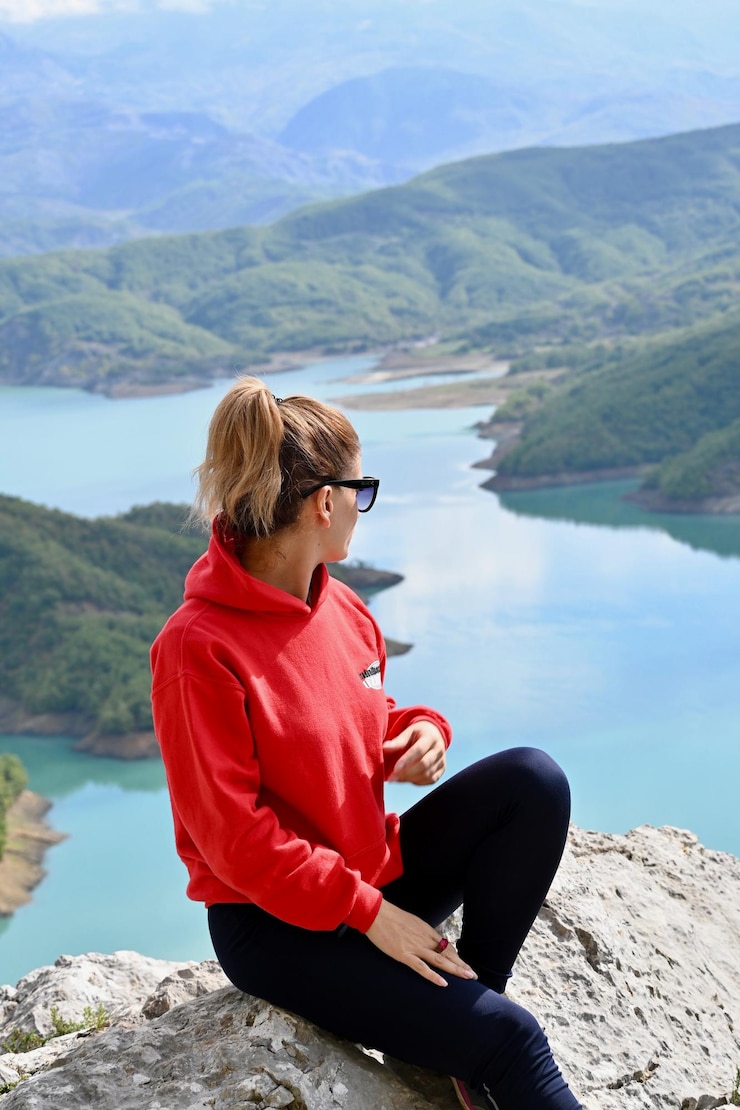 Foto mann sitzt auf einem felsen am see gegen berge