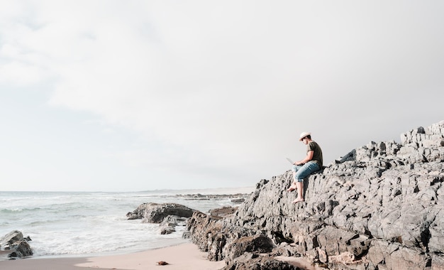 Mann sitzt auf einem Felsen am Strand mit Laptop allein und macht Remote-Arbeit