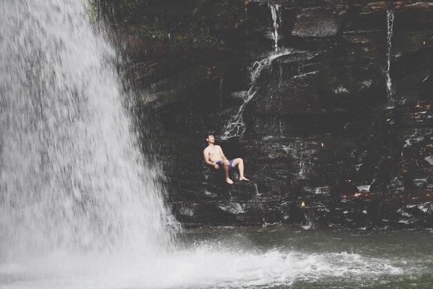 Foto mann sitzt auf einem felsen am wasserfall