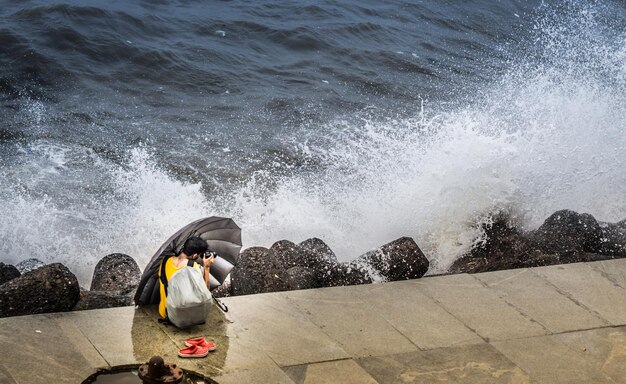 Foto mann sitzt auf einer stützmauer am meer