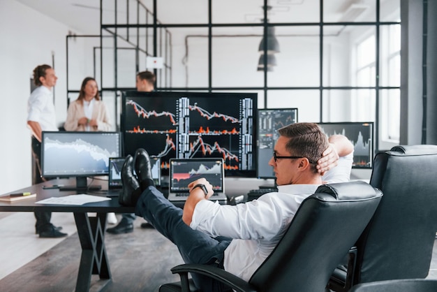 Mann sitzt auf Stuhl und macht Pause Das Team von Börsenmaklern arbeitet in einem modernen Büro mit vielen Bildschirmen