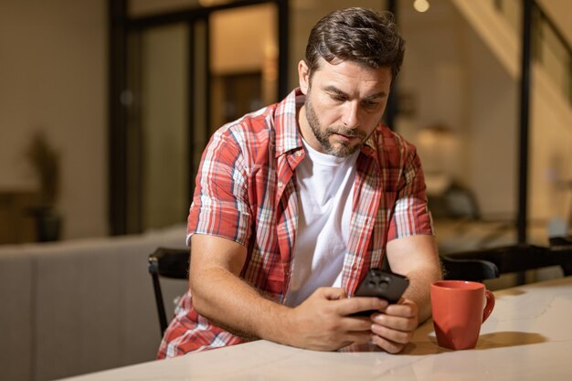 Mann sitzt entspannt auf der Couch und schaut auf sein Mobiltelefon. Reifer Mann benutzt Smartphone, um nachzuschauen