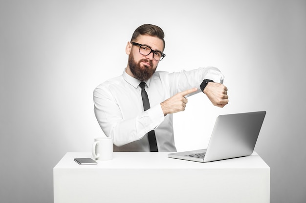 Mann sitzt im Büro und zeigt mit dem Finger auf seine Handuhr, die dir zeigt, dass die Zeit gekommen ist