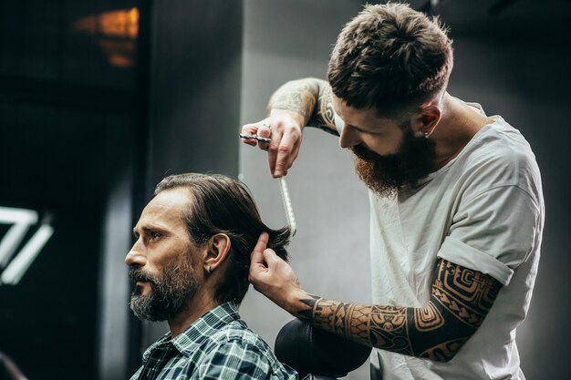 Mann sitzt im Sessel und aufmerksamer Friseur, der seinen Rücken beugt und Haare kämmt