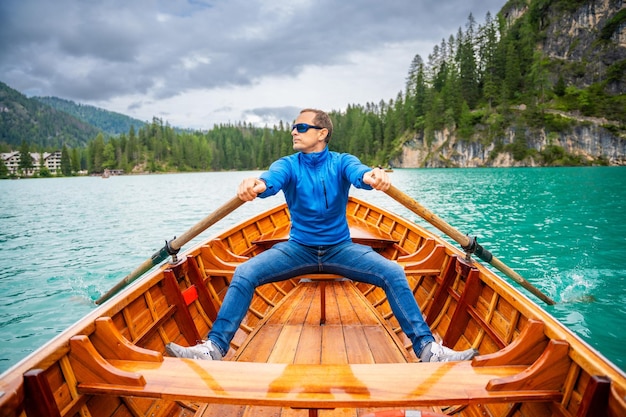Mann sitzt in einem großen braunen Boot am Lago di Braies Lake an einem bewölkten Tag in Italien Sommerferien in Europa
