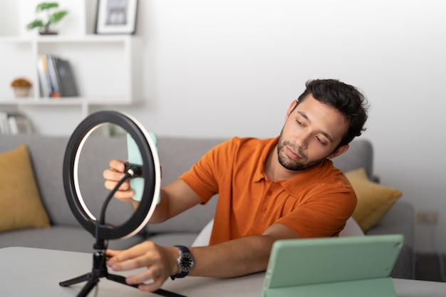 Mann sitzt in einem Wohnzimmer und richtet sein Handy ein, um im Ringlicht ein Selfie zu machen