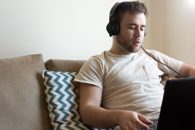 Mann sitzt mit Kopfhörern und Laptop auf dem Sofa